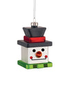 Colorful cube-shaped Snow Cube ornament by Alessi, with a black hat, white body, green base, and snowman facial features, hanging.