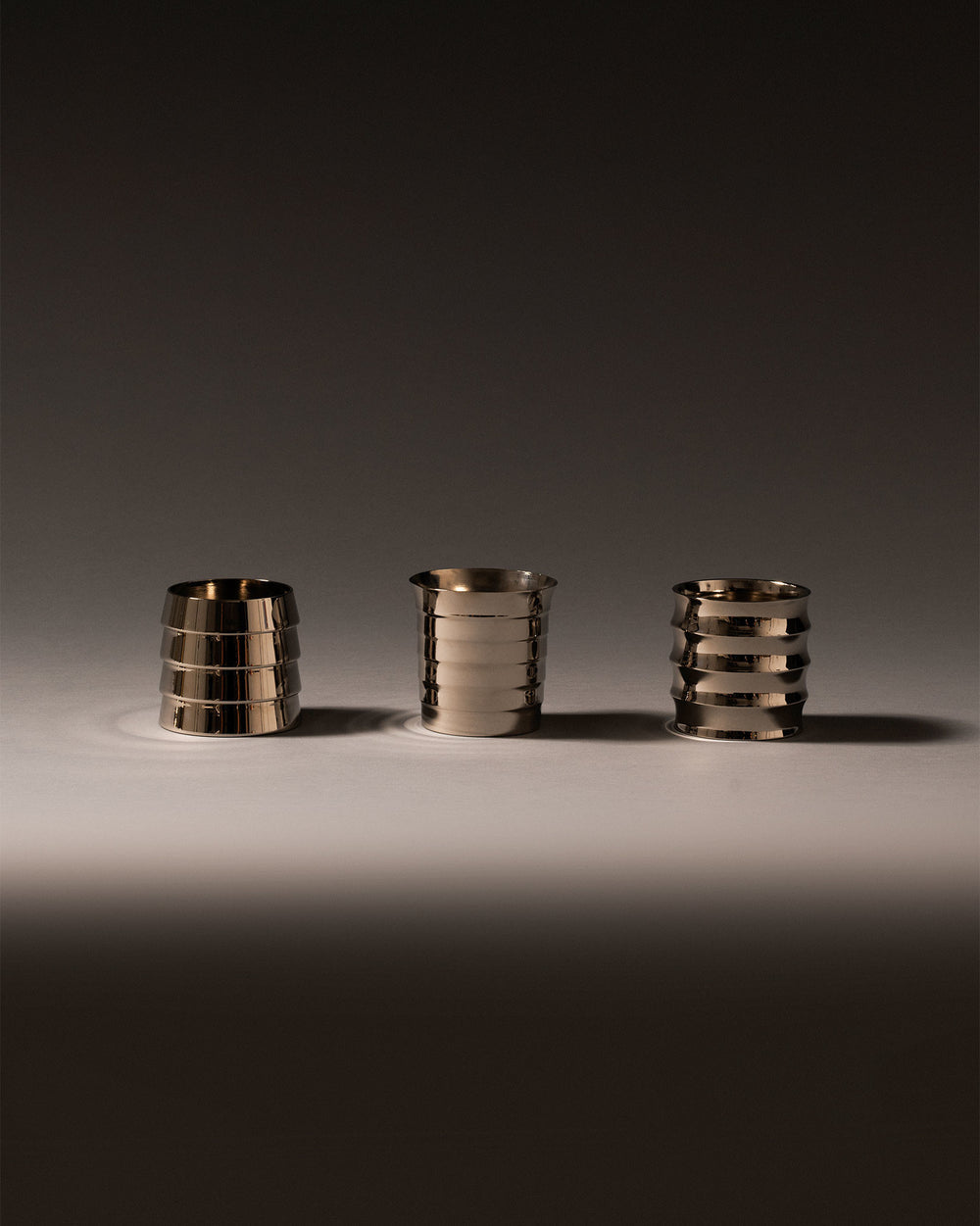 Metallic silver Dervisci glasses by Alessi, with three varying ribbed designs on a reflective surface.