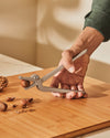 Grey metal nutcracker by Alessi, shaped like an alligator, cracking a hazelnut on a wooden board.