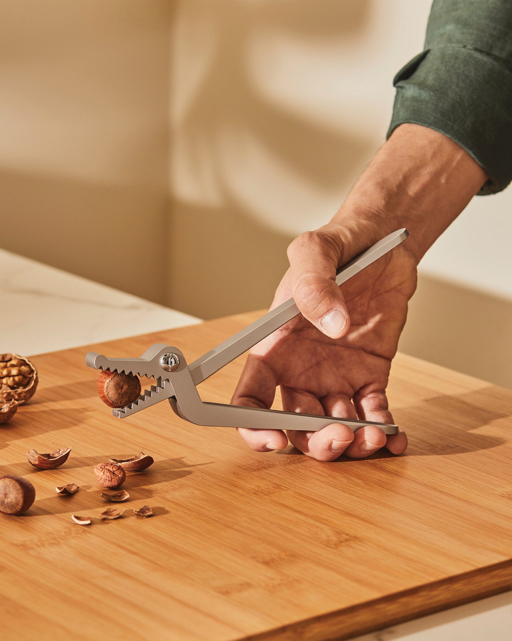 Grey metal nutcracker by Alessi, shaped like an alligator, cracking a hazelnut on a wooden board.