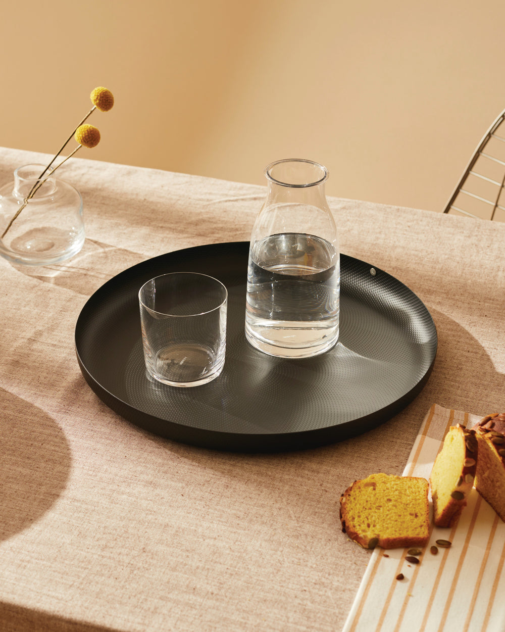 Black round textured tray by Alessi with a subtle dotted pattern, holding a glass and water carafe.