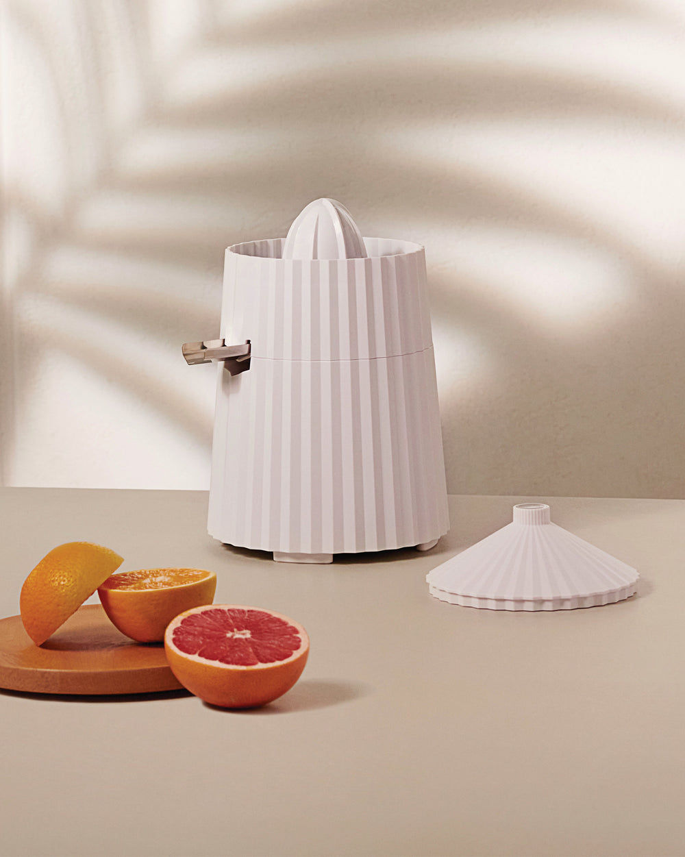 White pleated electric juicer by Alessi with a pour spout, displayed with fresh citrus halves.