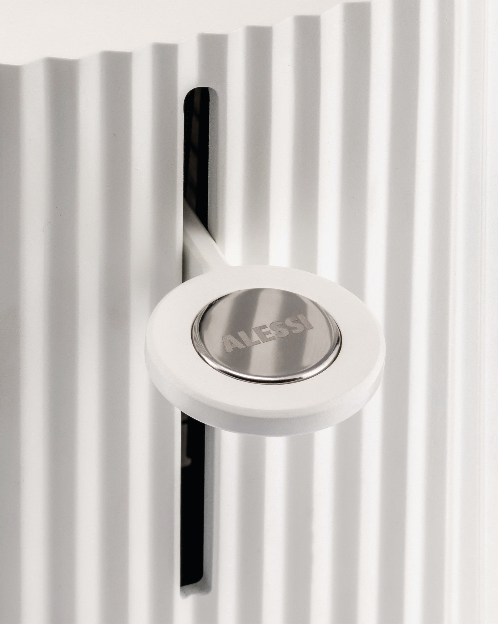 White pleated appliance by Alessi, with a round control lever and metallic logo plate.