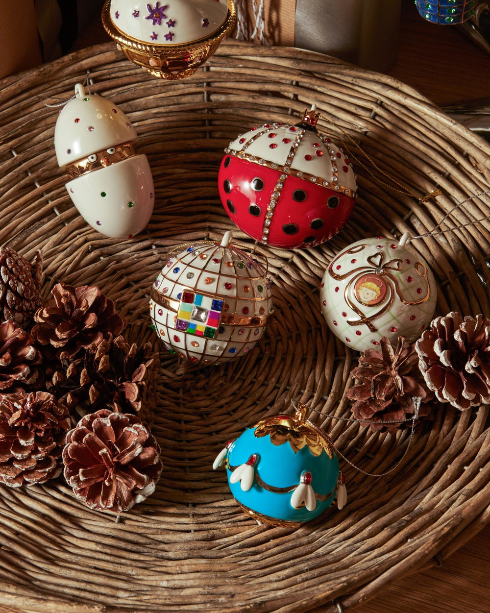A white and gold opening egg ornament by Alessi, embellished with colorful gems, displayed in a wicker basket.
