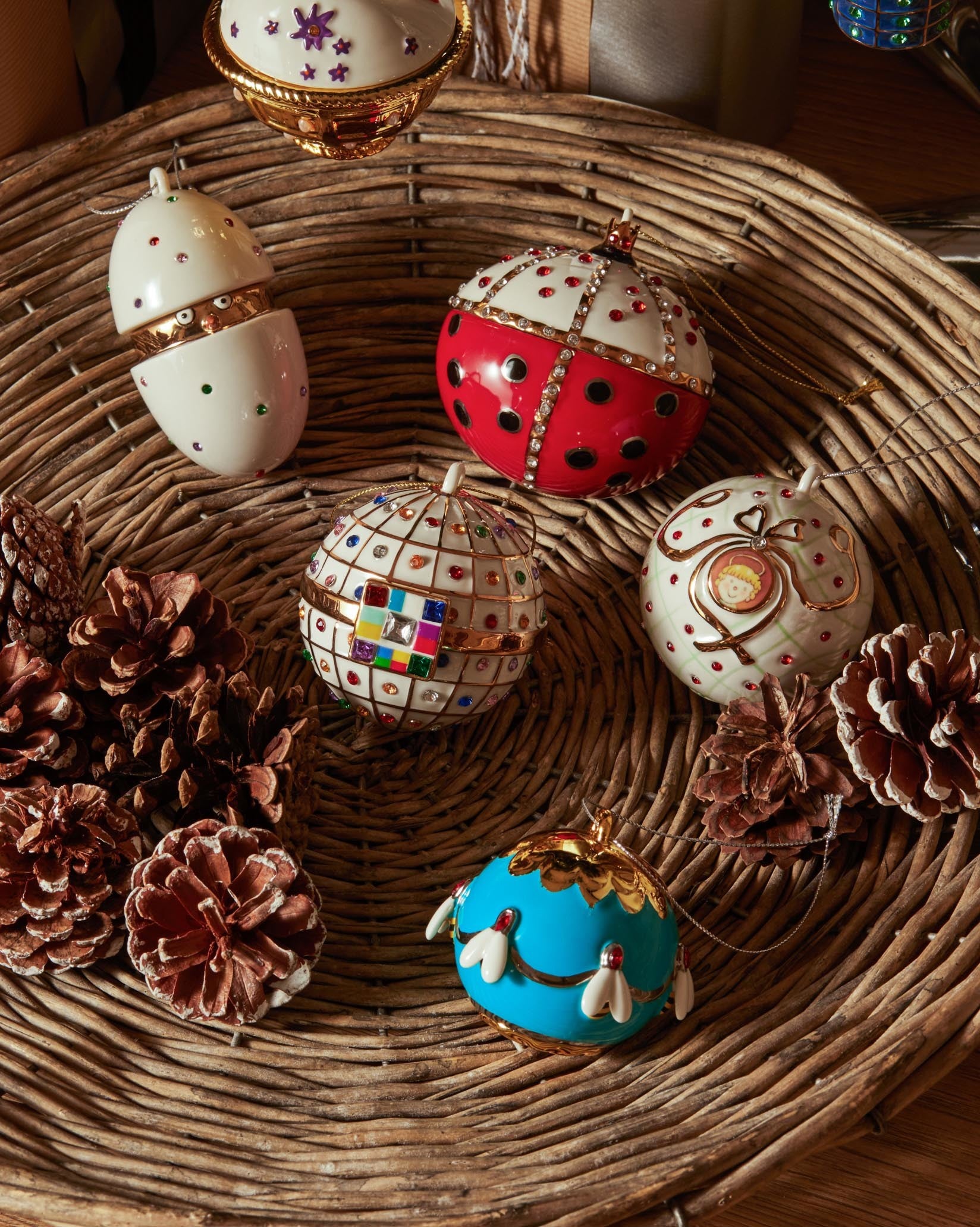 A white and gold opening egg ornament by Alessi, embellished with colorful gems, displayed in a wicker basket.