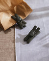 Dark grey cat-shaped bag clips by Alessi, one holding a brown paper bag on blue striped cloth.