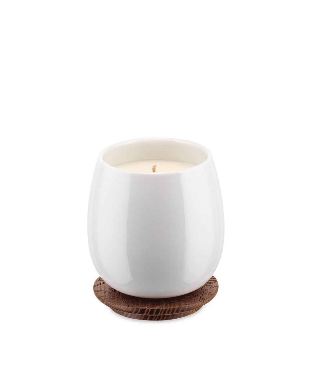 White ceramic candle by Alessi, resting on a brown wooden coaster with an engraved leaf pattern.