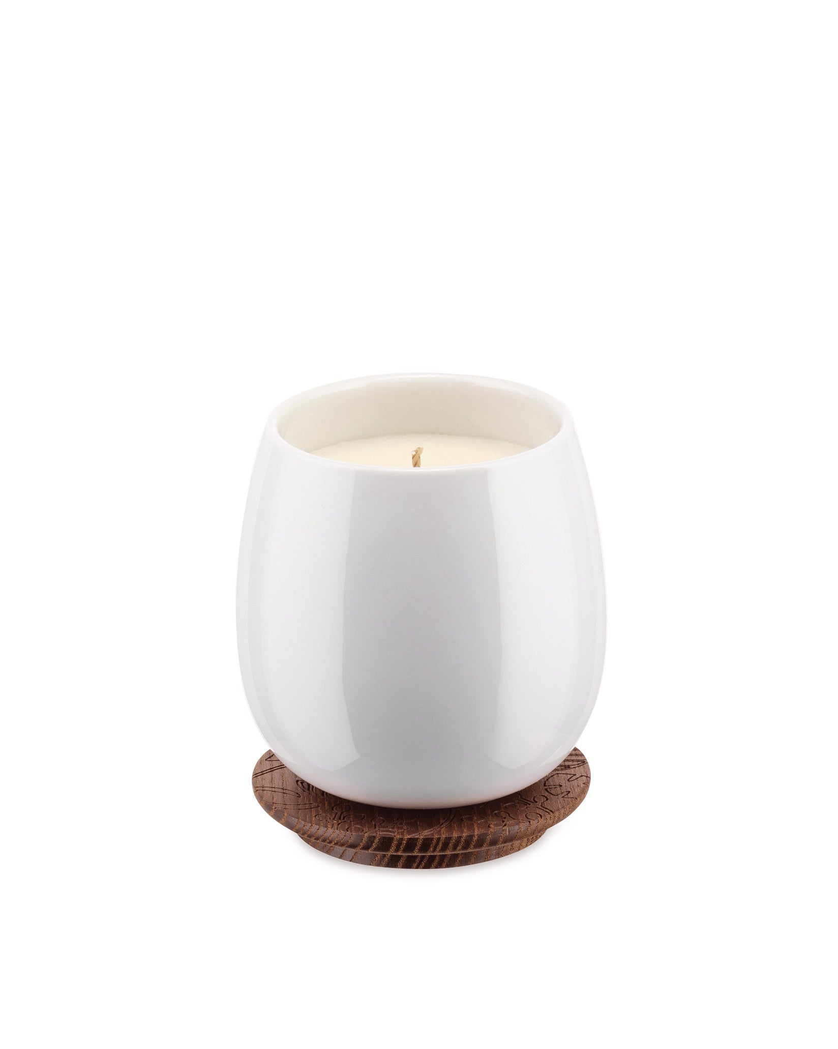 White ceramic candle by Alessi, resting on a brown wooden coaster with an engraved leaf pattern.