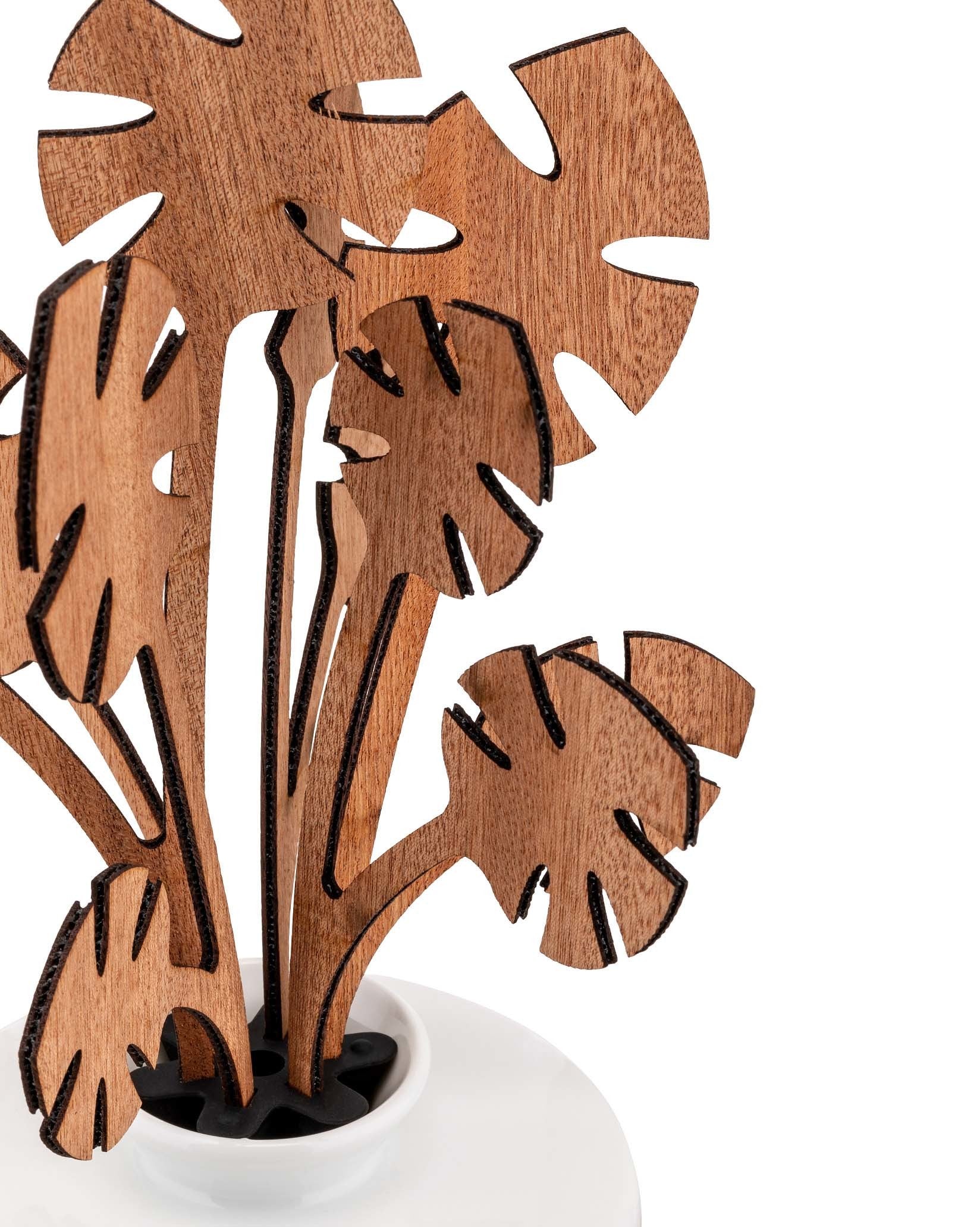 Brown wooden decorative plant by Alessi, featuring black-edged abstract monstera leaves in a white ceramic pot.