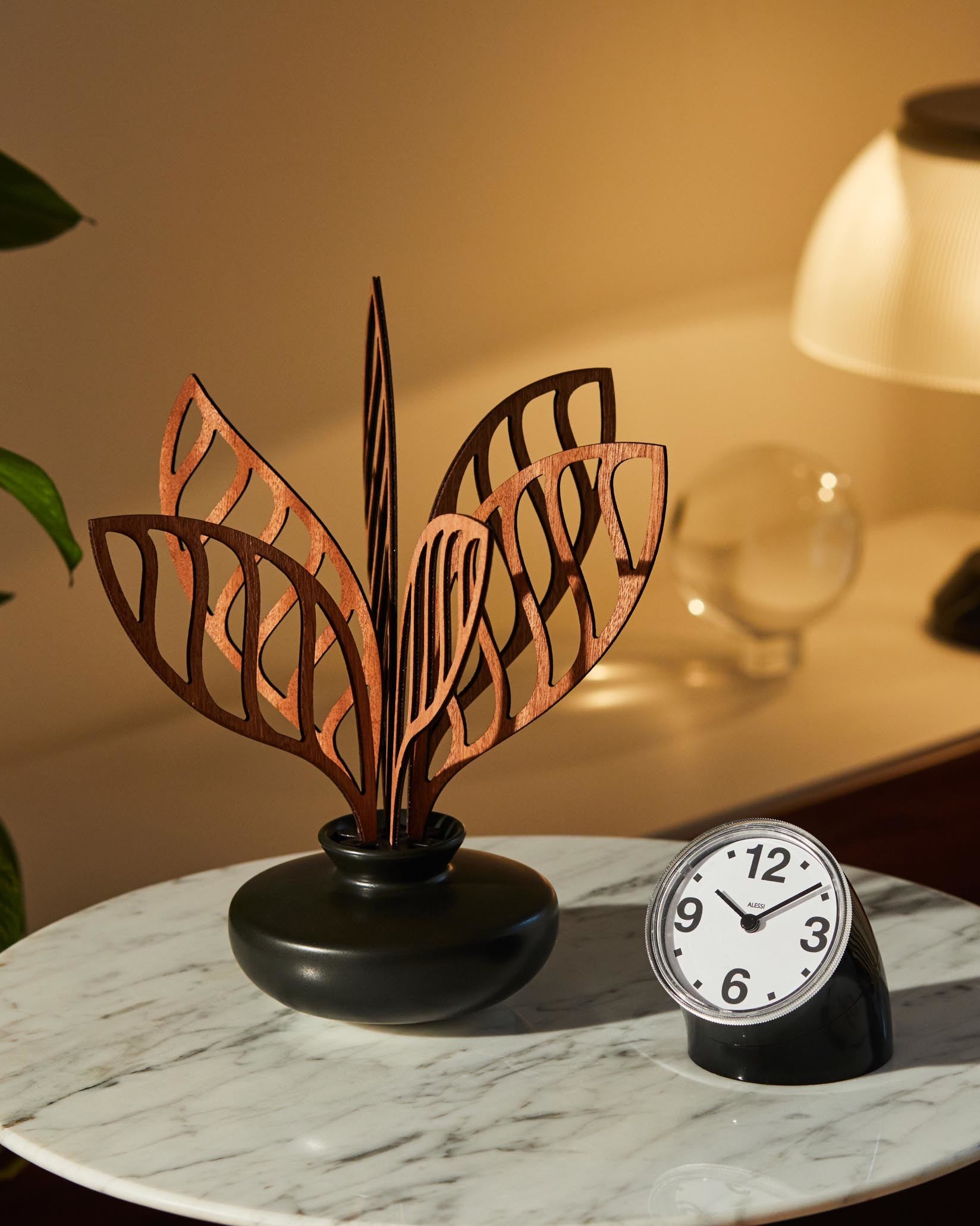 Wooden home fragrance diffuser by Alessi, featuring intricate leaf-like cutouts in a dark vase on a marble table.