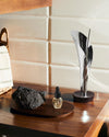 Chrome-plated abstract leaf incense holder by Alessi, with an incense stick, on a dark wooden surface.