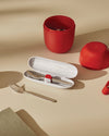Red portable food carrier and silver cutlery set by Alessi, with a white cutlery case and a notebook on a light tan surface.