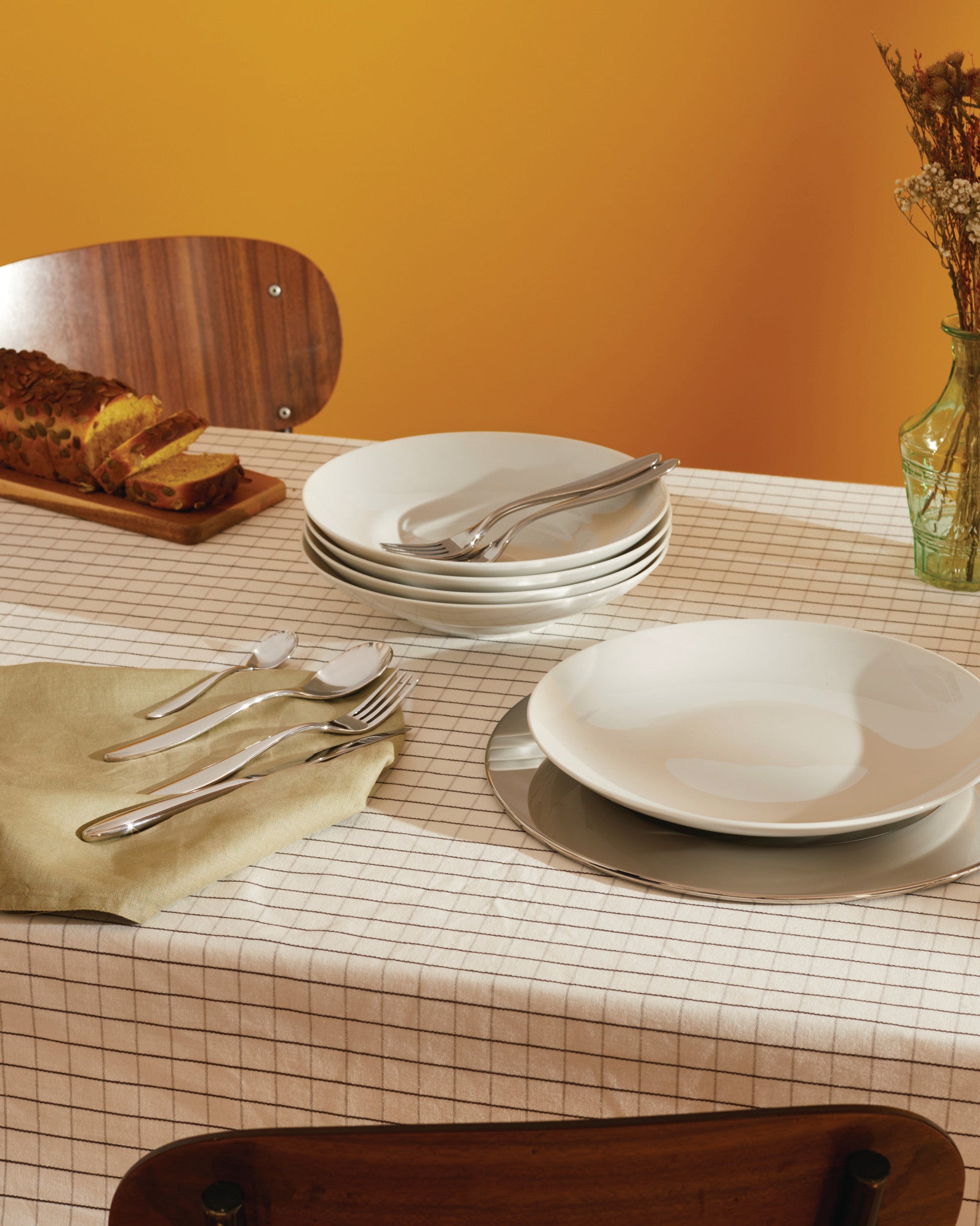Polished silver cutlery set by Alessi, including spoons, forks, and knives displayed on a light green napkin.