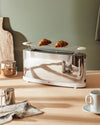 Long silver chrome toaster by Alessi with a white base and two croissants on a warming rack.