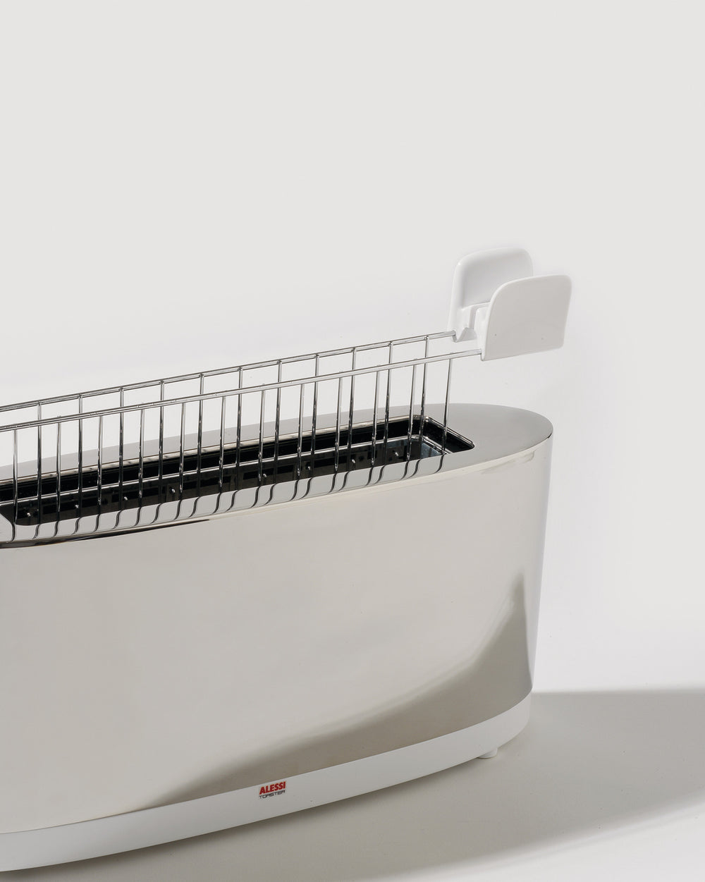 Polished stainless steel toaster by Alessi with a single long slot and a white removable warming rack.