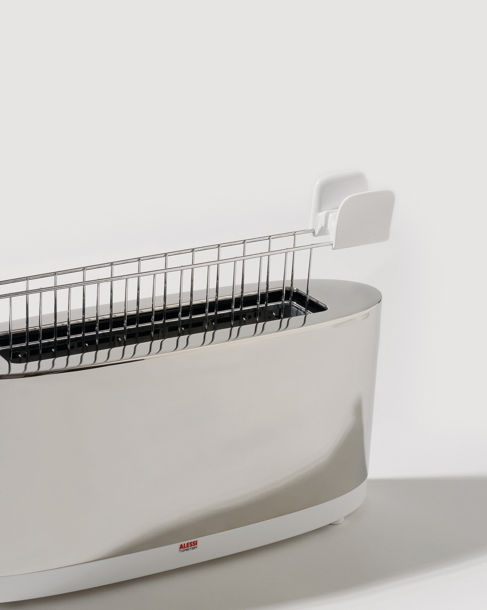 Polished stainless steel toaster by Alessi with a single long slot and a white removable warming rack.