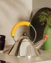 Stainless steel whistling kettle by Alessi with a yellow handle and a red bird-shaped spout.